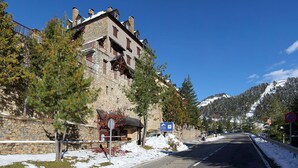 Un bâtiment en pierre doté d’un balcon, un panneau indiquant un parking et, au loin, une montagne enneigée.