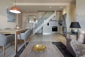 A modern kitchen with a central island, a dining area with a wooden table and grey chairs, and a staircase leading to an upper level. - Pujolo by FeelFree Rentals (Baqueira)