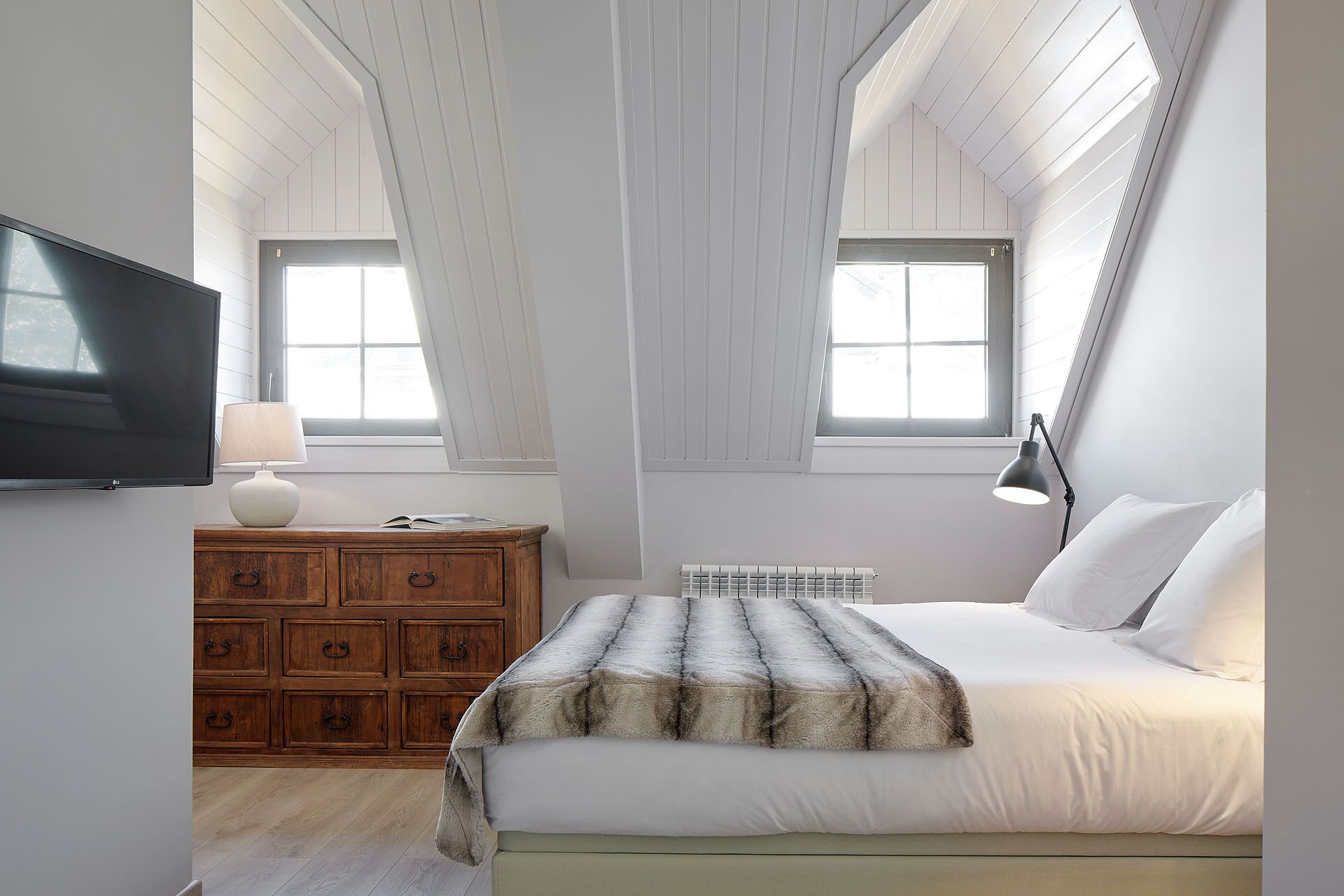 Une chambre à coucher avec un lit, une télévision, une commode en bois et une fenêtre.