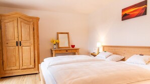 A hotel room with a wooden wardrobe, a bedside table with a mirror, a lamp, and a bed with white bedding. - Alm Appartement für 2 Personen (Berchtesgaden)