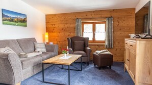 A cozy room with a wooden wall, a sofa, a chair, a small table, and a cabinet. - Alm Appartement für 2 Personen (Berchtesgaden)