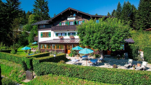 A two-story chalet with a balcony, surrounded by lush greenery and trees. - Alm Appartement für 2 Personen (Berchtesgaden)