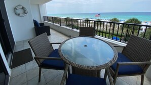 A balcony with wicker chairs and a glass table, overlooking a beach with umbrellas and a flag. - "Breakers East 304" Gulf Front 2BR/2BA Beach setup included (Destin)