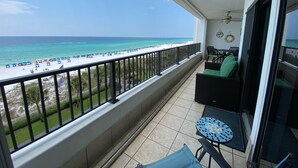 A balcony with a view of a beach, a table with chairs, and a small round table with a mosaic top. - "Breakers East 502" Gulf Front 2BR/2BA Beach setup included (Destin)