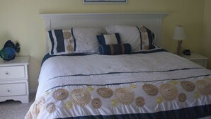 Een net opgemaakt bed met een bloemenprint, een wit hoofdbord en een schilderij erboven.