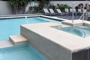 A swimming pool with steps leading into it, surrounded by lounge chairs and plants.