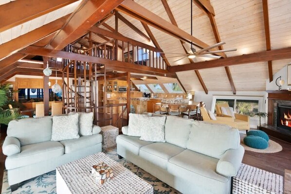 Un loft spacieux avec de hauts plafonds, des poutres apparentes, un coin salon confortable avec des canapés et une table basse, un espace cuisine et une cheminée.