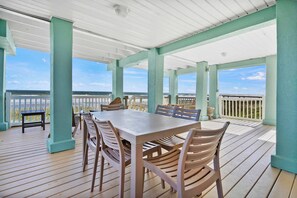 A covered outdoor deck with a wooden table and chairs, a small bench, and a view of the ocean.