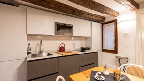A modern kitchen with grey cabinets, a wooden ceiling, and a dining area with a table and chairs. - “Ea casa de mì - The Magic of Experiencing Venice” (Venezia)