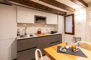A modern kitchen with grey cabinets, a wooden ceiling, and a dining area with a table and chairs. - “Ea casa de mì - The Magic of Experiencing Venice” (Venezia)