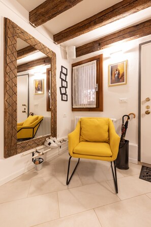 A room with a yellow armchair, a large mirror, a radiator, and a door with a wooden frame. - “Ea casa de mì - The Magic of Experiencing Venice” (Venezia)