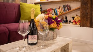 A table with two wine glasses and a bottle of wine, a vibrant flower arrangement, and a bookshelf with books and figurines in a cozy room. - “Ea casa de mì - The Magic of Experiencing Venice” (Venezia)