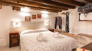 A bedroom with a wooden ceiling, a bed with a patterned bedspread, a bedside table, and a wall-mounted coat rack. - “Ea casa de mì - The Magic of Experiencing Venice” (Venezia)