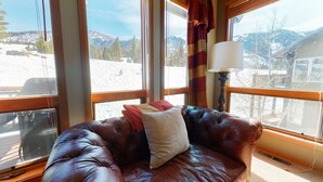A leather couch with a cushion and a lamp, positioned by a window with a view of a snowy landscape. - Snowcreek V 774 Gorgeous Mountain Views with Private Garage, Washer Dryer and Gas Grill by RedAwning (Mammoth Lakes)