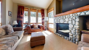 A cozy living room with a stone fireplace, leather sofas, and a large window with curtains. - Snowcreek V 774 Gorgeous Mountain Views with Private Garage, Washer Dryer and Gas Grill by RedAwning (Mammoth Lakes)
