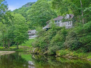 A house surrounded by lush greenery and a calm body of water. - Riverfront Sanctuary | Your Mountain Getaway (Burnsville)