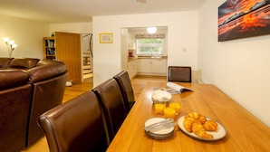 Un comedor con una mesa de madera dispuesta para el desayuno, con croissants y zumo de naranja. Se observan sillas de cuero y una estantería al fondo.