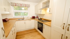 Una cocina compacta con armarios blancos, encimera de madera, horno integrado y ventana con vistas a zonas verdes.