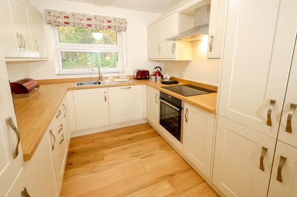 A compact kitchen with white cabinets, a wooden countertop, a built-in oven, and a window with a view of greenery.
