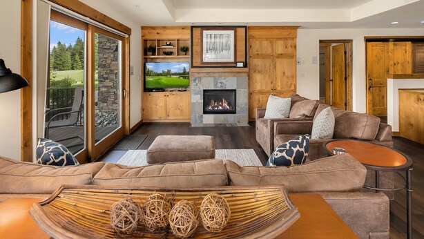 Een moderne woonkamer met een stenen openhaard, een grote flatscreen-tv en een gezellige zithoek met een bruine leren bank en voetenbank.