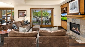 Een gezellige woonkamer met een open haard, een zithoek en uitzicht op een terras met tuinmeubilair.