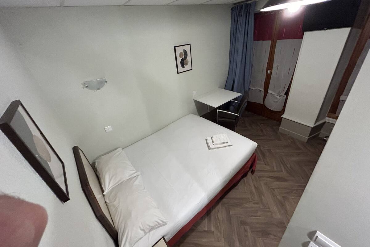 Ein kleines, aufgeräumtes Schlafzimmer mit Bett, Schreibtisch und Kleiderschrank.