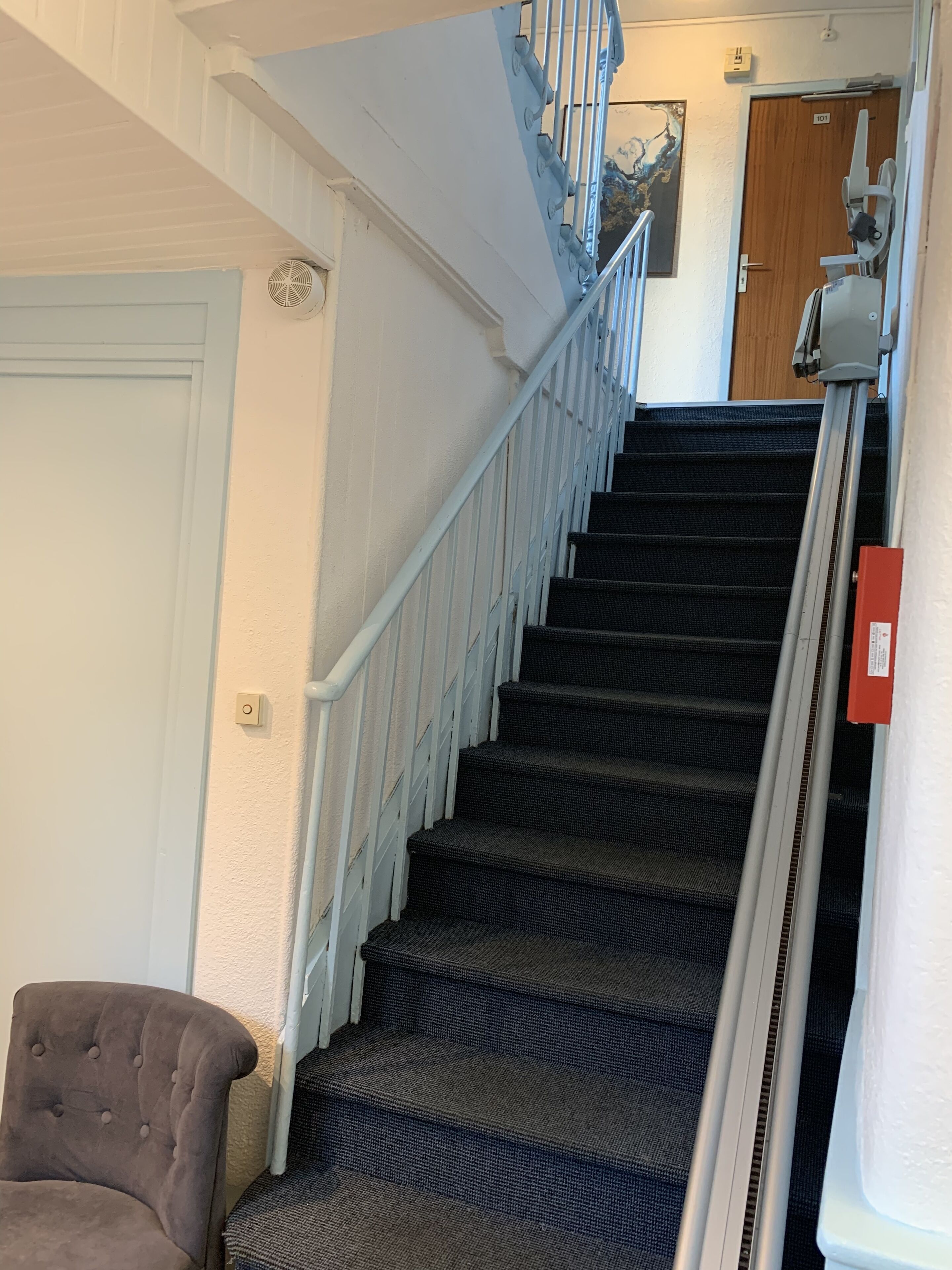 A staircase with a handrail, carpeted steps, and a door at the top.