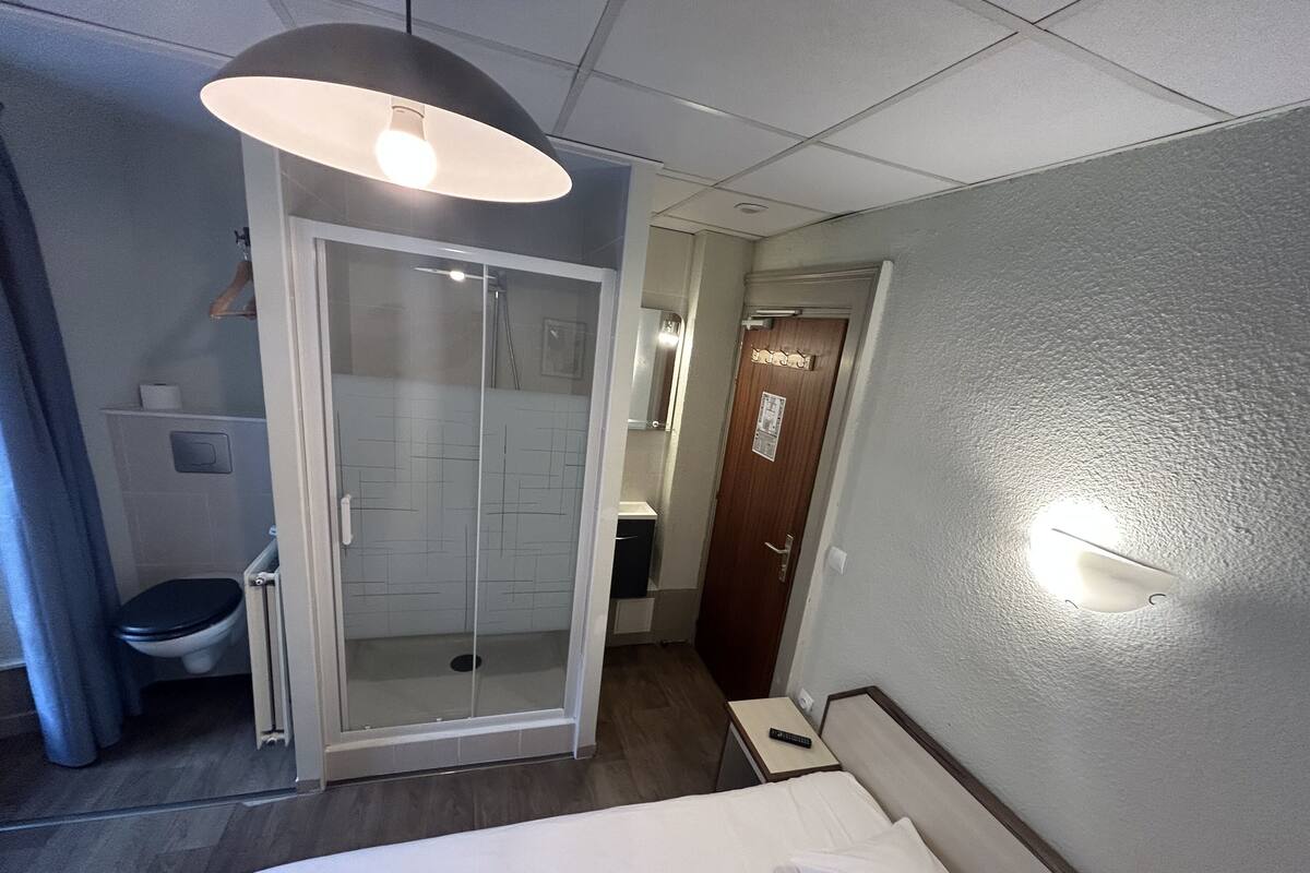 Ein Hotelzimmer mit Bett, Duschbereich, Toilette und einer Tür zu einem anderen Raum.