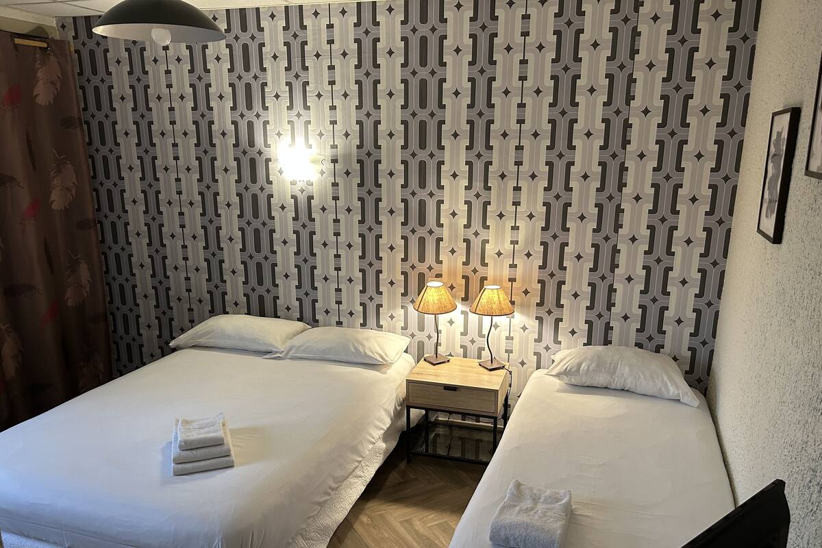 Ein Hotelzimmer mit zwei Betten, einem gemusterten Wandteppich und einem Nachttisch mit Lampen.