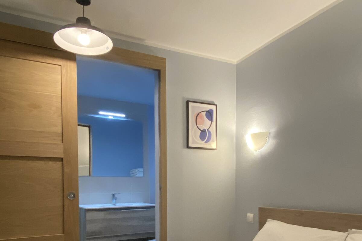Ein Schlafzimmer mit einem Bett, einem Holzschrank, einem Badezimmer mit Spiegel und einer Wandleuchte.