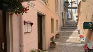 A narrow cobblestone alley with a building labeled "HOTEL BROISIN RESTAURANT" on the left. There are potted plants and a mailbox on the right.