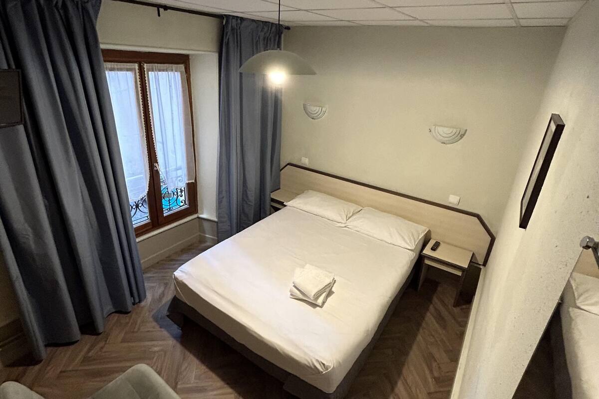 Ein Hotelzimmer mit Bett, Schreibtisch, Stuhl und einem Fenster mit Vorhängen.