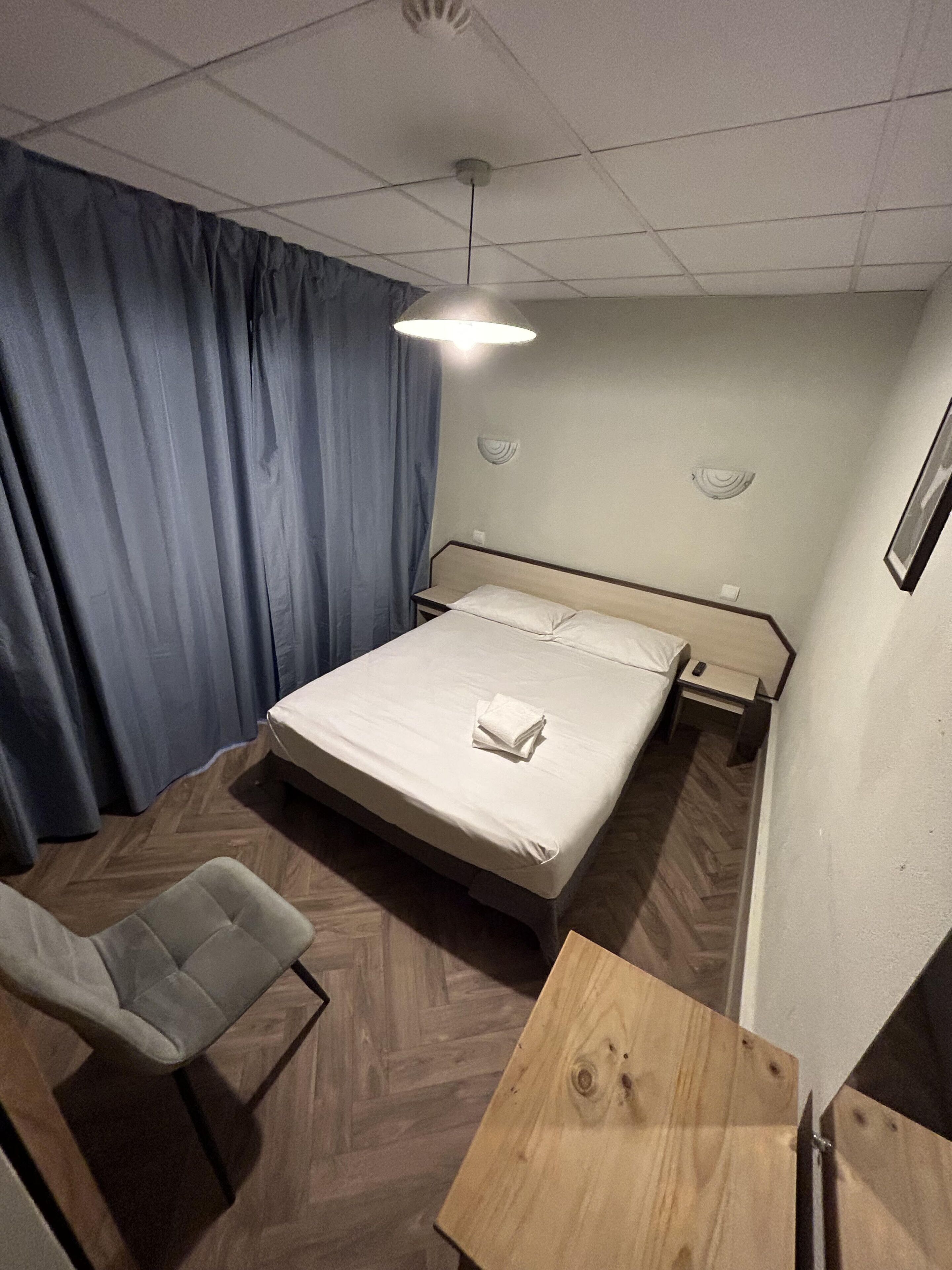 Ein Hotelzimmer mit einem Bett, einem Sessel, einem Holztisch und einer Deckenleuchte.