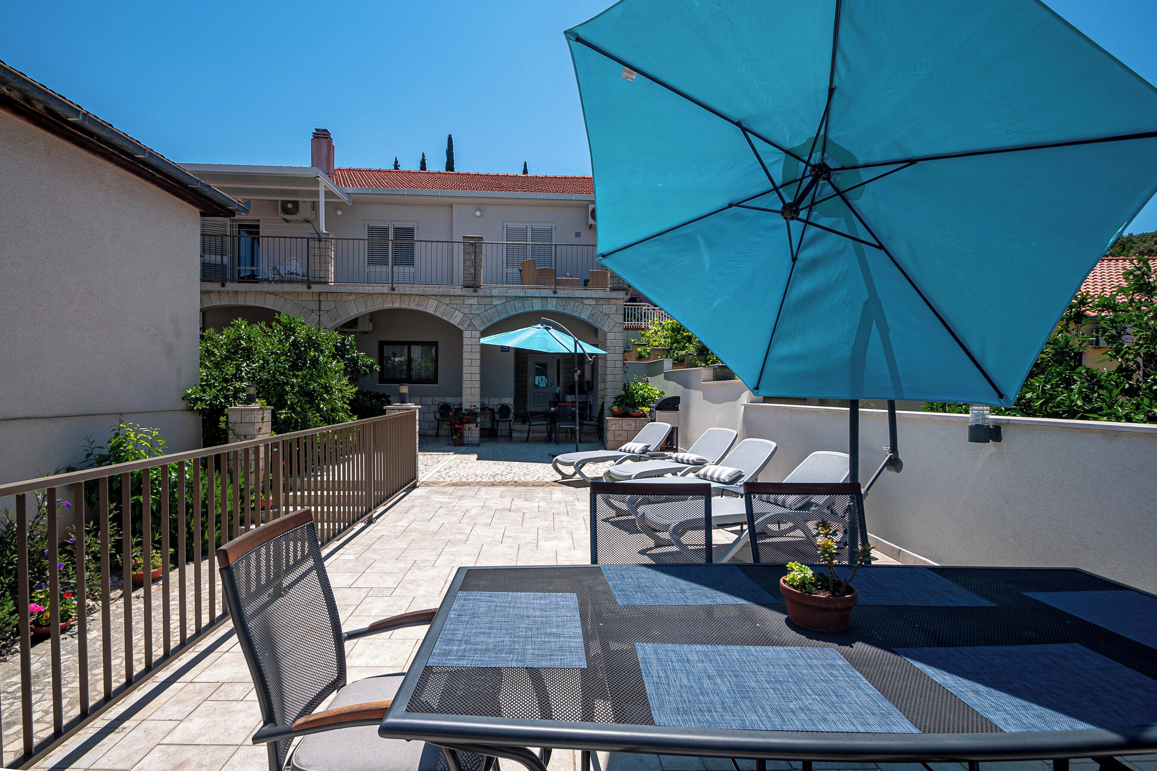 Een terras met buitenmeubilair, een tafel en een grote parasol.