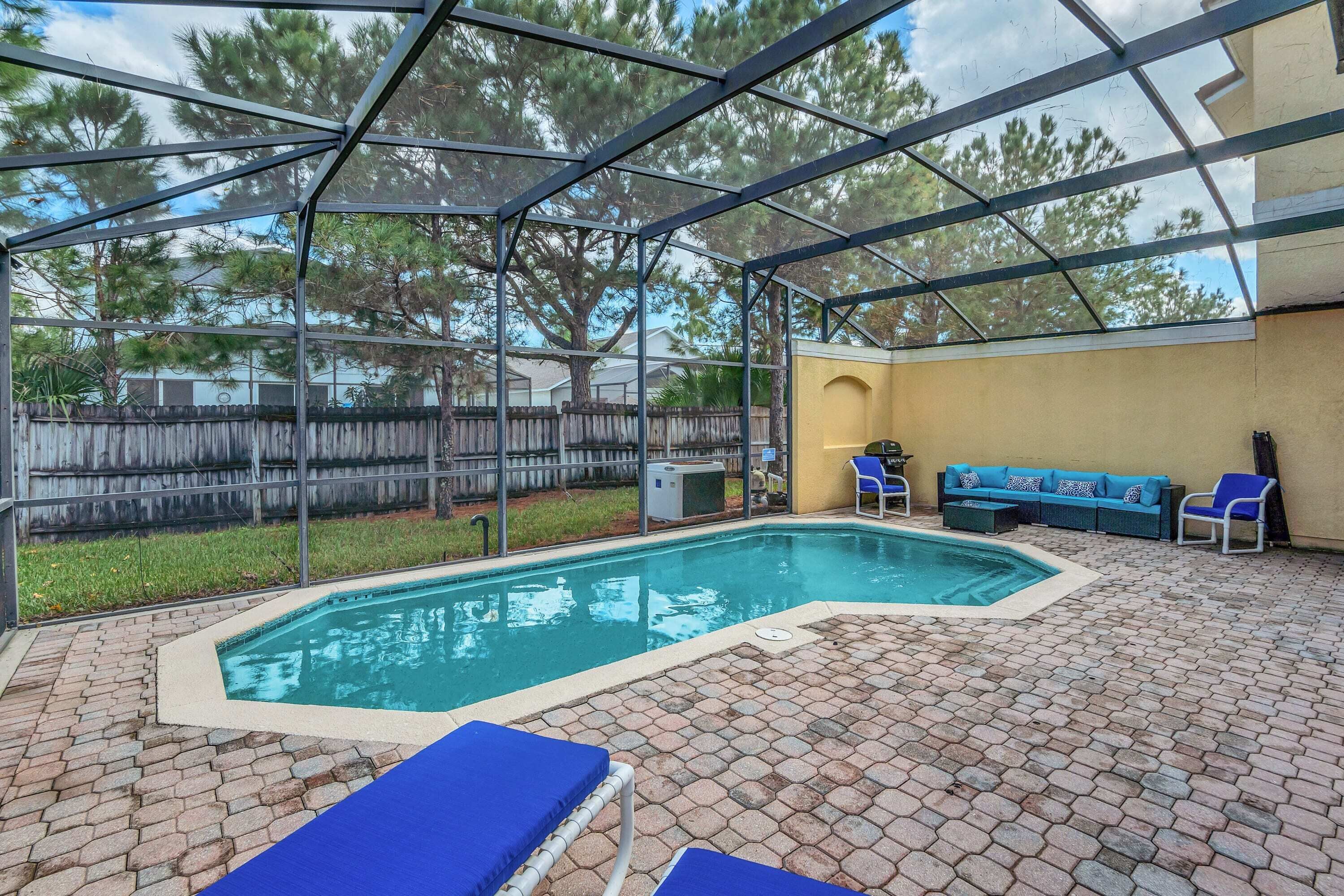 A covered outdoor swimming pool with blue lounge chairs and a yellow wall.