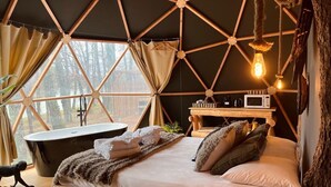 Un dormitorio acogedor tipo casa en un árbol, con una cama grande, un escritorio de madera, una bañera y vistas al bosque a través de amplios ventanales.