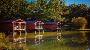 Cabañas de madera con ventanas de vidrio construidas sobre un lago tranquilo, rodeadas de árboles.