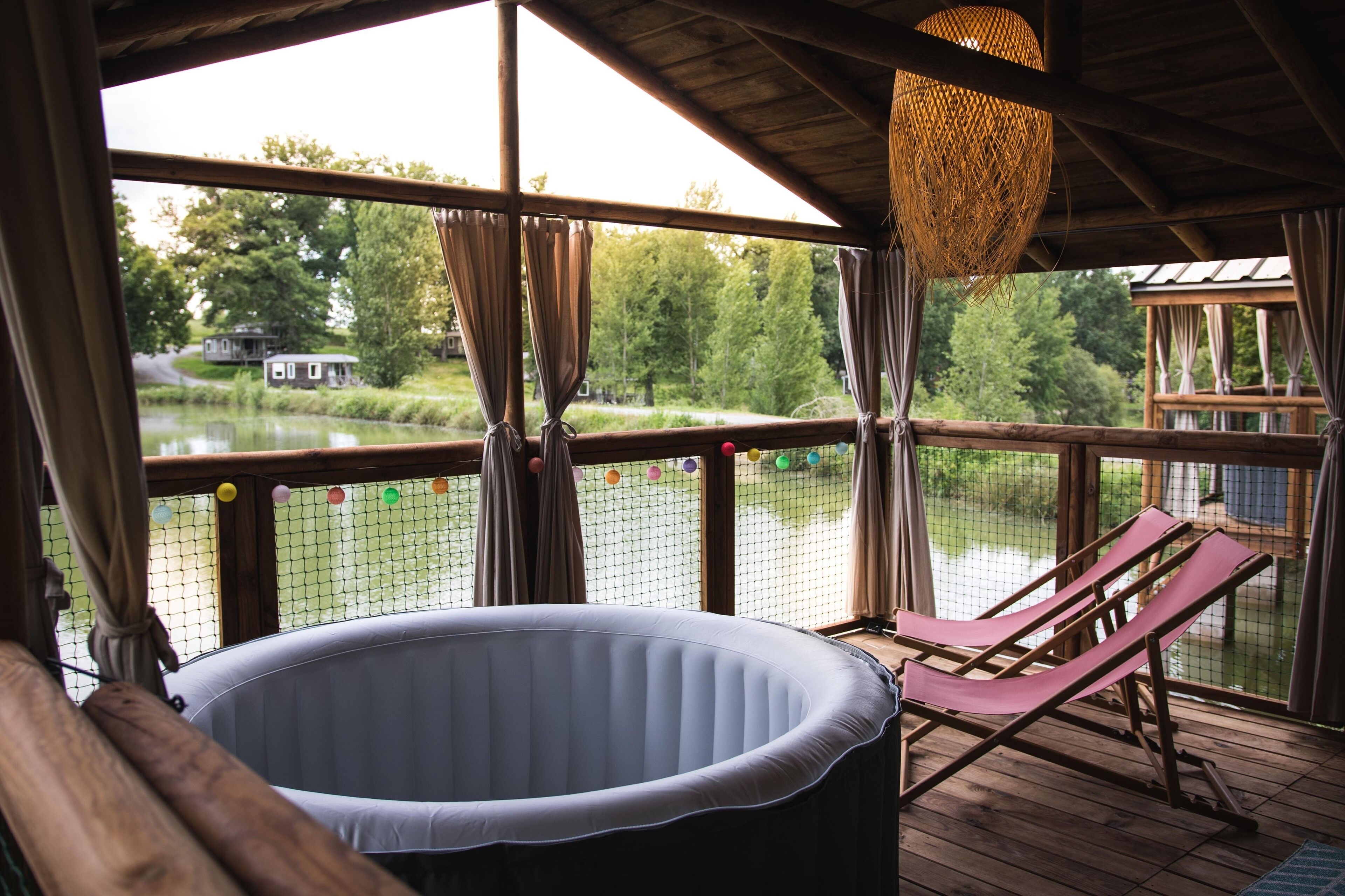Un espace extérieur abrité comprenant un jacuzzi, des chaises longues et une vue sur un lac.