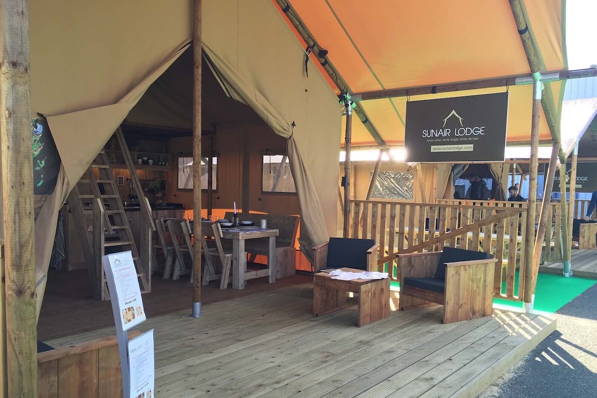 A wooden deck with a table and chairs, a tent with a sign reading "SUNAFIRE LODGE", and a wooden staircase leading to an upper level.