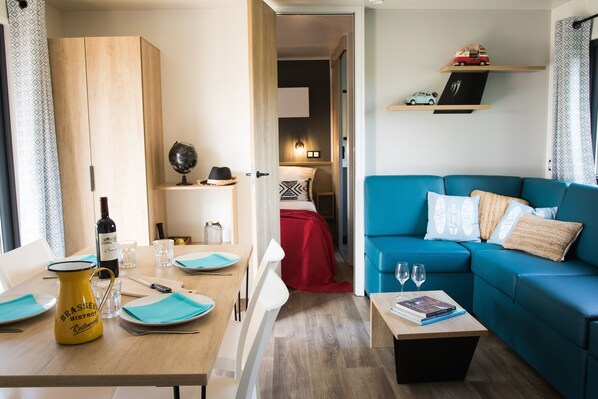 A modern living room with a blue sofa, a dining table with blue placemats, and a coffee table with books and glasses. - Whaka Lodge (Seissan)