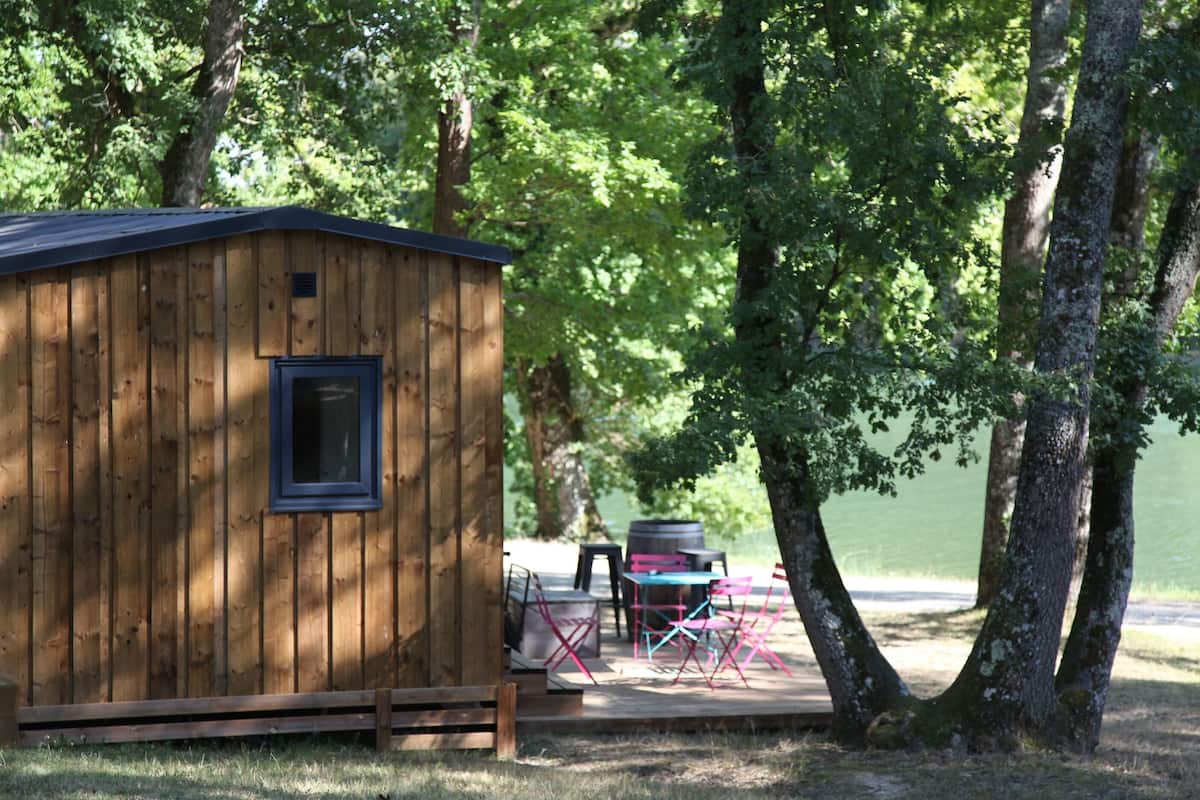A wooden cabin with a window, surrounded by trees and a lake.