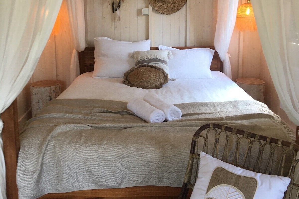 A cozy bed with a canopy, a woven basket, and a dreamcatcher on the wall.