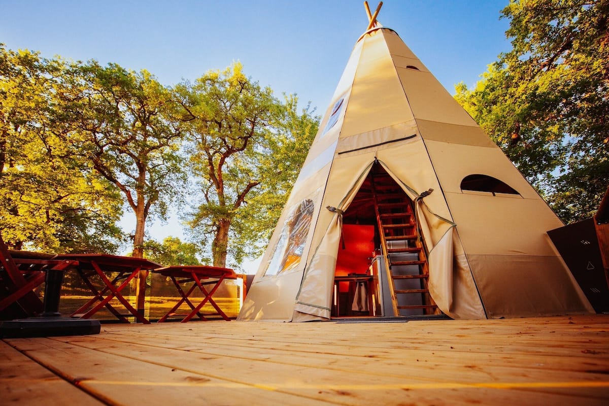 A conical tent with a ladder leading to a door, set on a wooden deck with a picnic table nearby.
