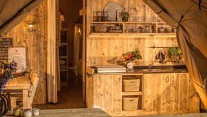 Una tienda acogedora y rústica con interior de madera, que incluye una kitchenette con estantes, un lavamanos y diversos utensilios de cocina.