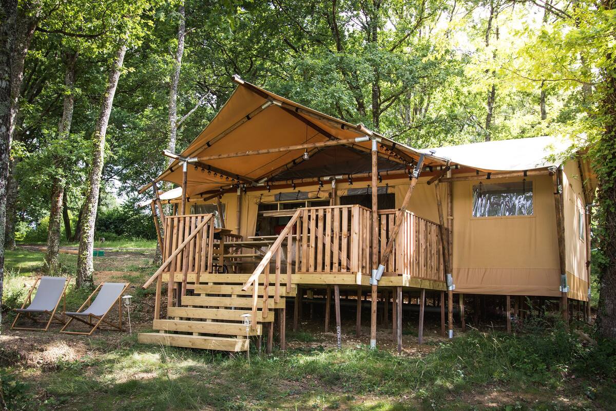 A wooden cabin with a balcony and stairs, surrounded by trees.