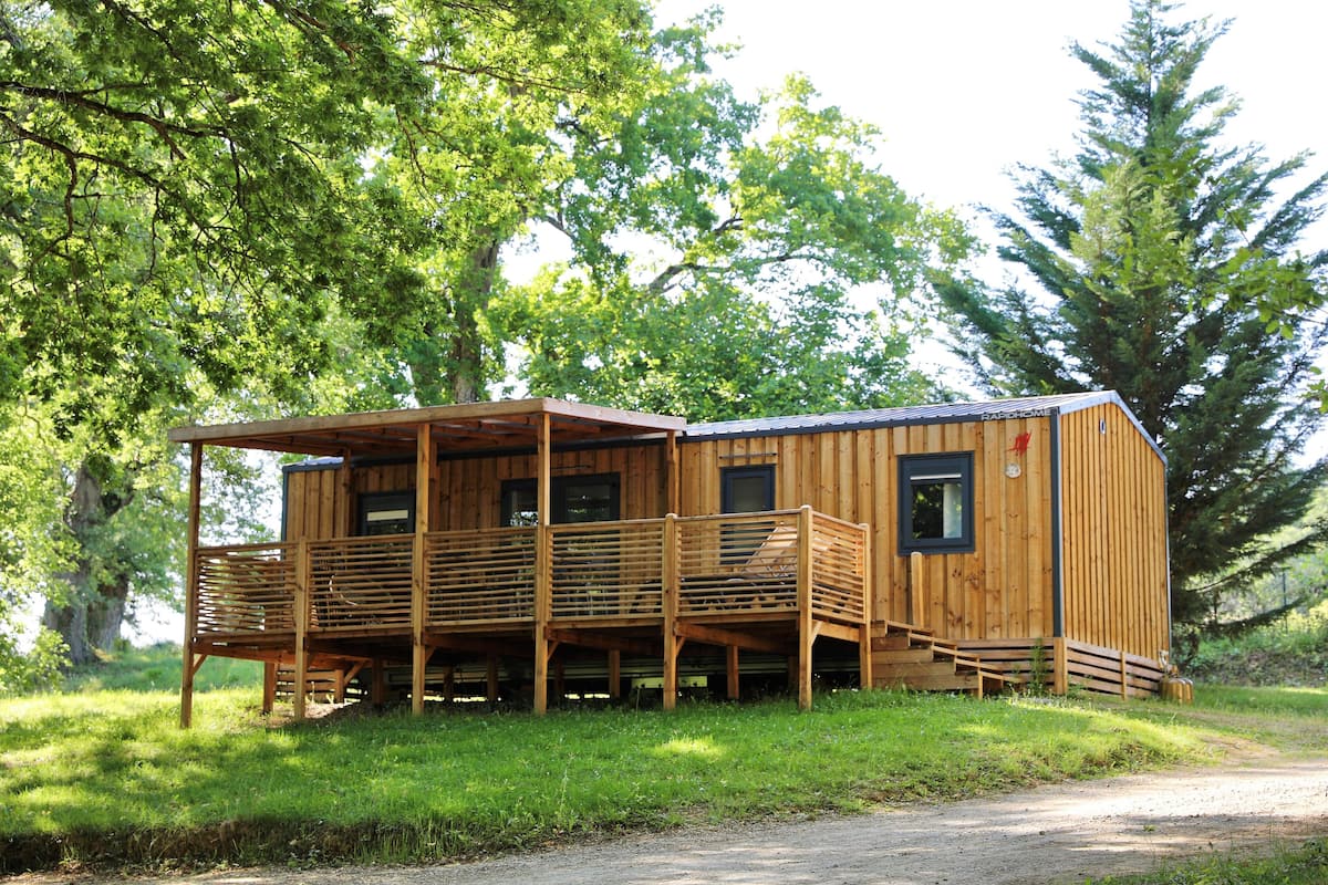 A wooden cabin with a balcony and a covered porch, surrounded by trees.