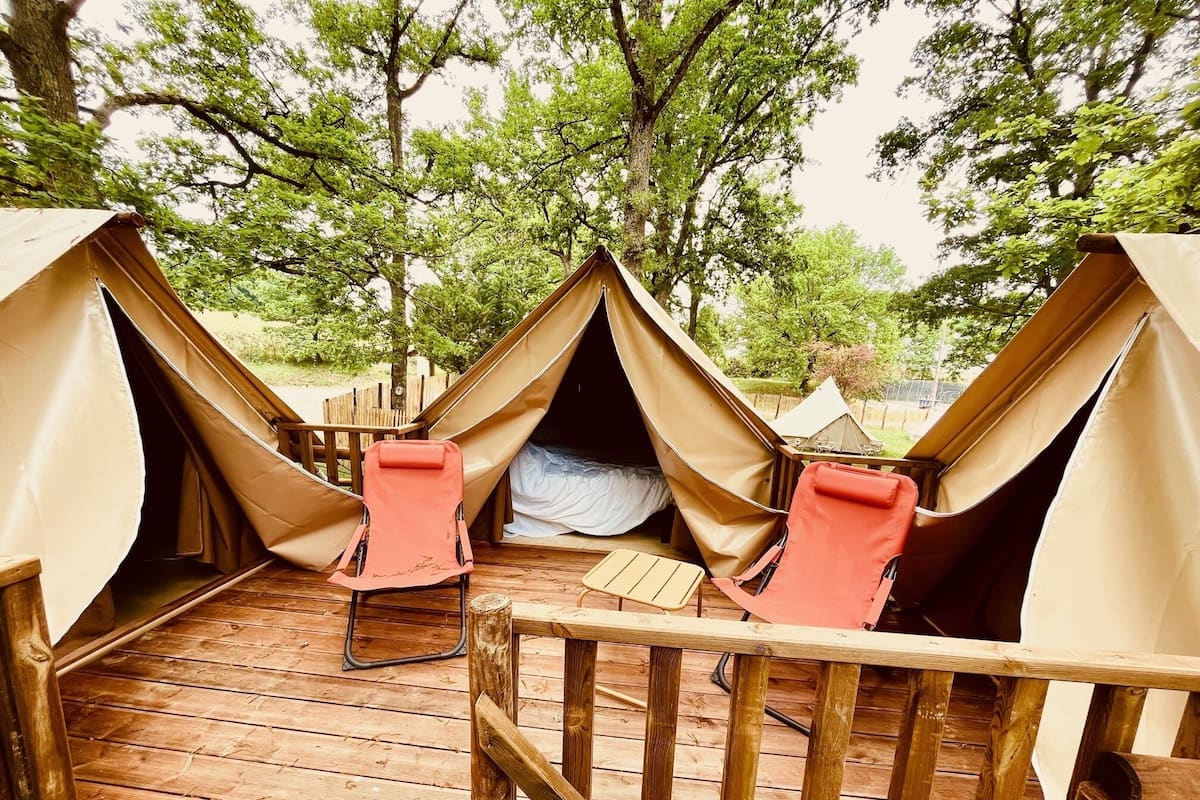 A campsite with two tents, each with a single red chair and a wooden deck.