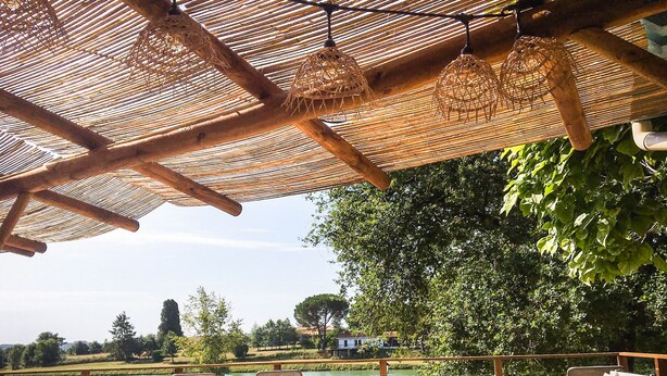 Un área de estar al aire libre con muebles de madera y sombrillas de paja, con vista a un cuerpo de agua y follaje.