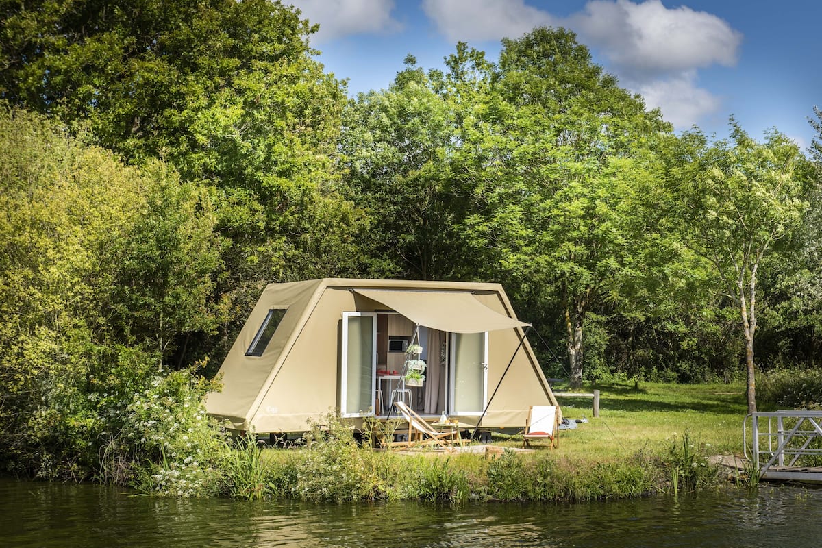 A tented accommodation by a lake surrounded by trees.