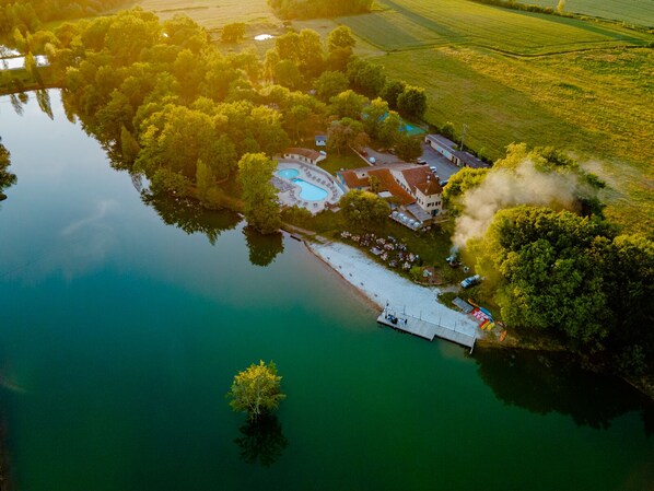An aerial view of a lakeside property with a swimming pool, a dock, and a building with a red roof. - Whaka Lodge (Seissan)
